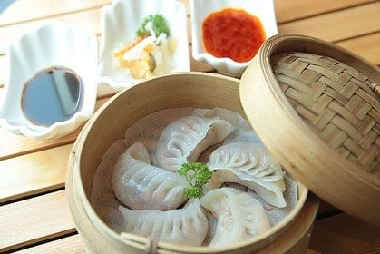 Steamed dumplings in bamboo basket with sauces.