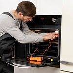 Technician repairing an oven in a kitchen.