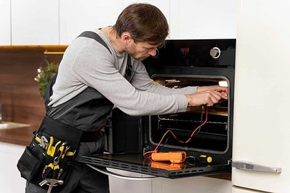 Technician repairing an oven in a kitchen.