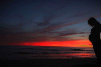 Silhouette of pregnant woman at sunset on beach.