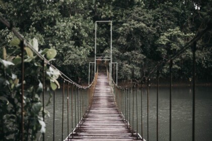 Suspension bridge over tranquil river surrounded by greenery.