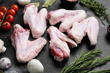Uncooked turkey wings with herbs and tomatoes on stone.