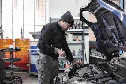 Mechanic troubleshooting a cars overheating issue in a workshop.