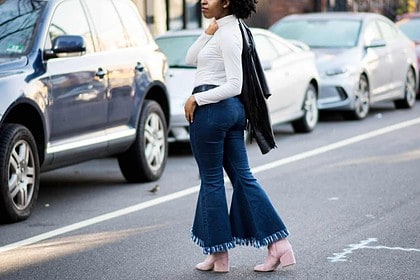 Woman modeling flared jeans with sandals on city street.