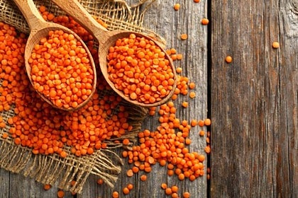 Red lentils displayed in wooden spoons on rustic table.
