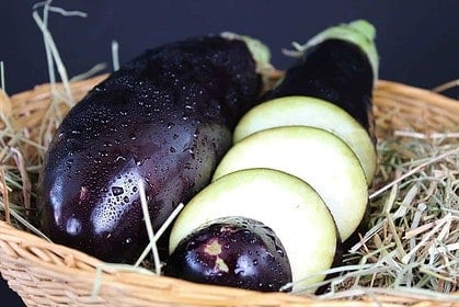 Sliced and whole eggplants in basket, cooking preparation.