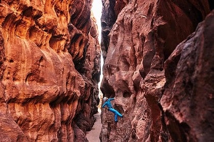 Climber ascending narrow canyon with essential gear.