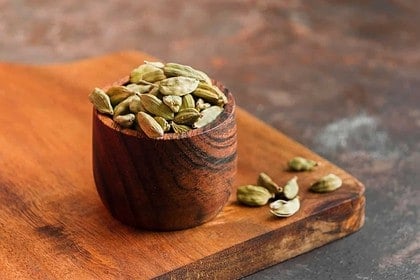 Cardamom pods in wooden bowl on kitchen board.