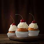 Cherry cream cupcakes on rustic wood backdrop.