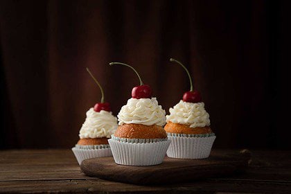 Cherry cream cupcakes on rustic wood backdrop.