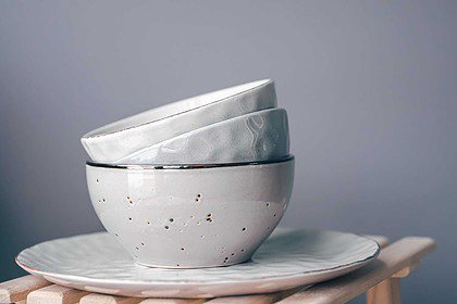Stacked pastel bowls and plates on wooden stand with grey backdrop.