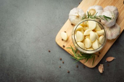 Garlic and herbs infused oil in glass jar on wooden surface.