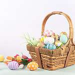 Assorted pastel Easter eggs in a basket on a wooden surface.