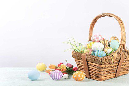 Assorted pastel Easter eggs in a basket on a wooden surface.