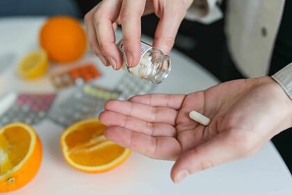 Person holding a vitamin D pill, with halved oranges in the background.