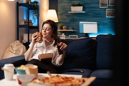 Woman enjoying burger on couch with movie snacks.