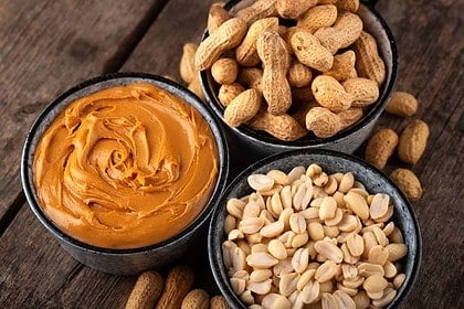 Peanut butter and shelled peanuts on a wooden surface.