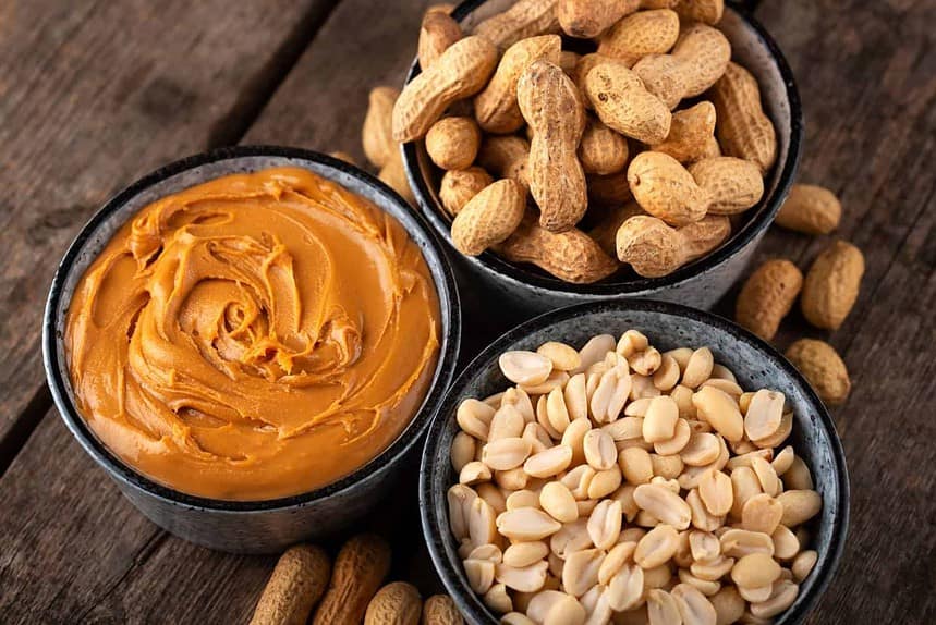 Peanut butter and shelled peanuts on a wooden surface.