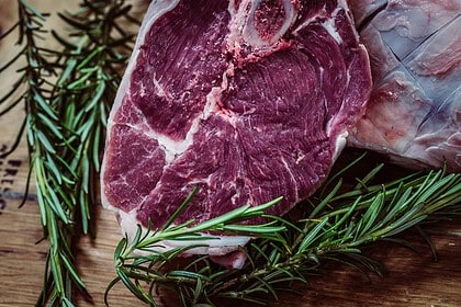 Raw venison heart with rosemary on wooden cutting board.