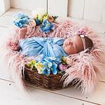 Newborn asleep in flower basket, soft textures surrounding.