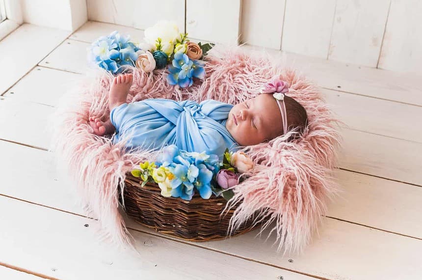 Newborn asleep in flower basket, soft textures surrounding.